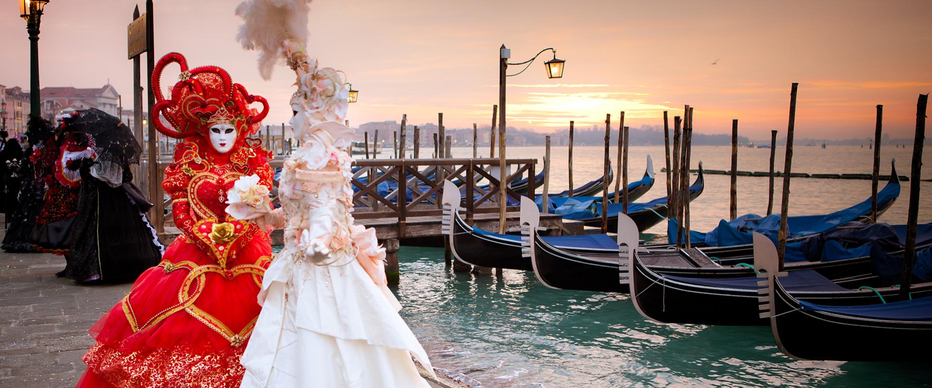 Maschere veneziane colorate sul lungomare al tramonto, con gondole sullo sfondo.