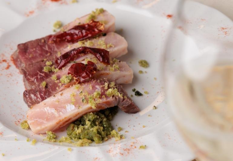 Fette di carne con peperoncini secchi e granella verde su piatto bianco.